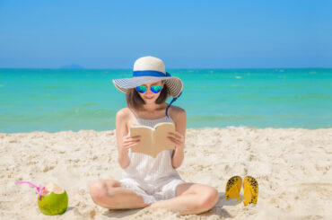 Eine Frau sitzt am Strand und liest ein Buch.