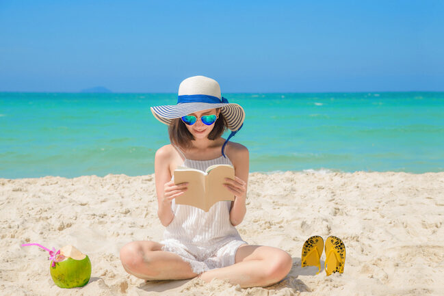 Eine Frau sitzt am Strand und liest ein Buch.