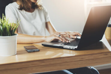 Eine Frau sitzt am Schreibtisch und arbeitet am Laptop.