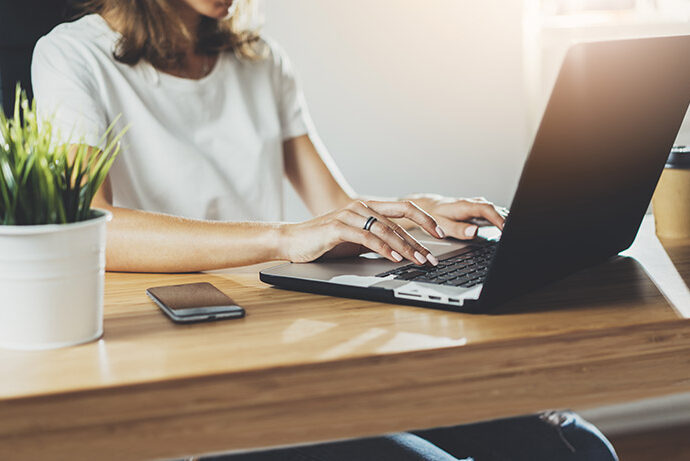 Eine Frau sitzt am Schreibtisch und arbeitet am Laptop.